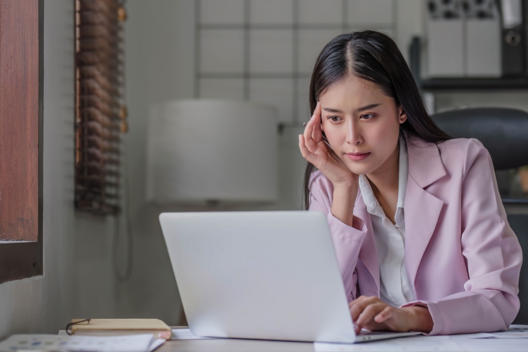 A woman at her computer, thinking carefully.